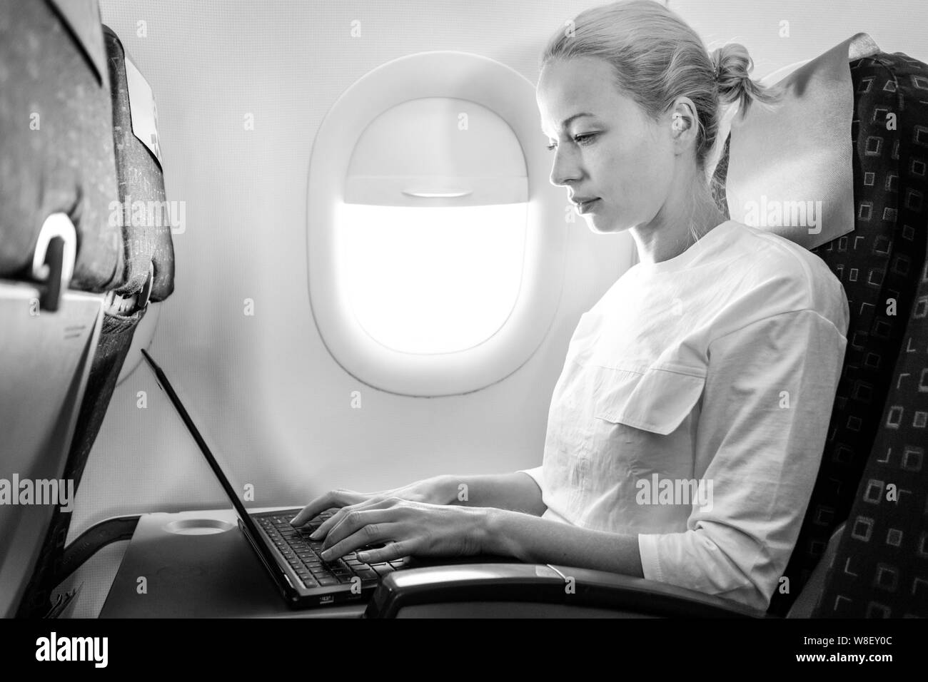 Attractive caucasian female passenger working at modern laptop computer using wireless connection on board of commercial airplane flight Stock Photo