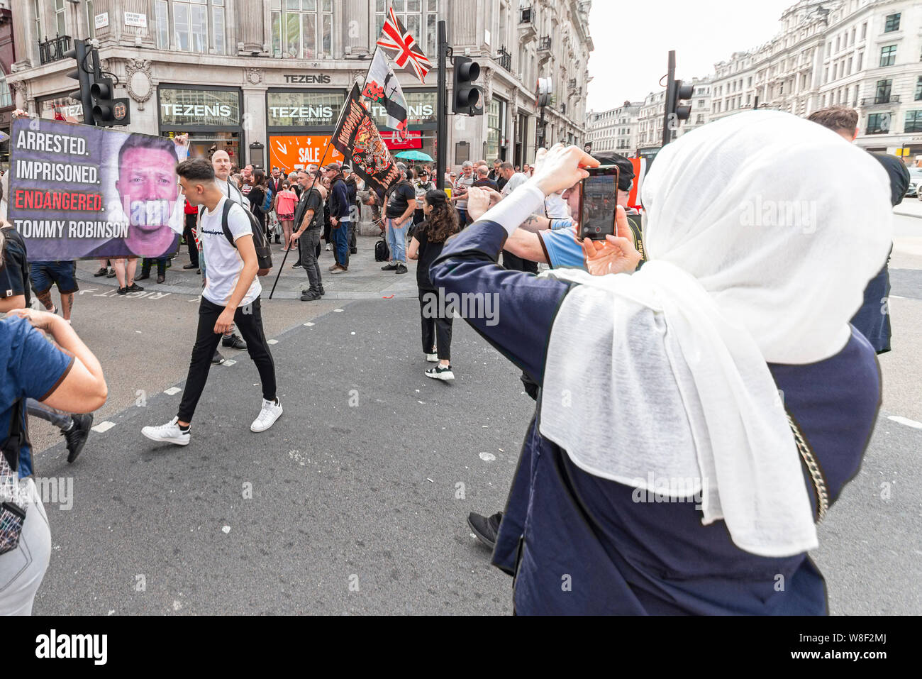 Female in head scarf taking a photograph of protesters at a Tommy Robinson protest rally In London, UK. Possibly Muslim hijab. Gagged banner Stock Photo