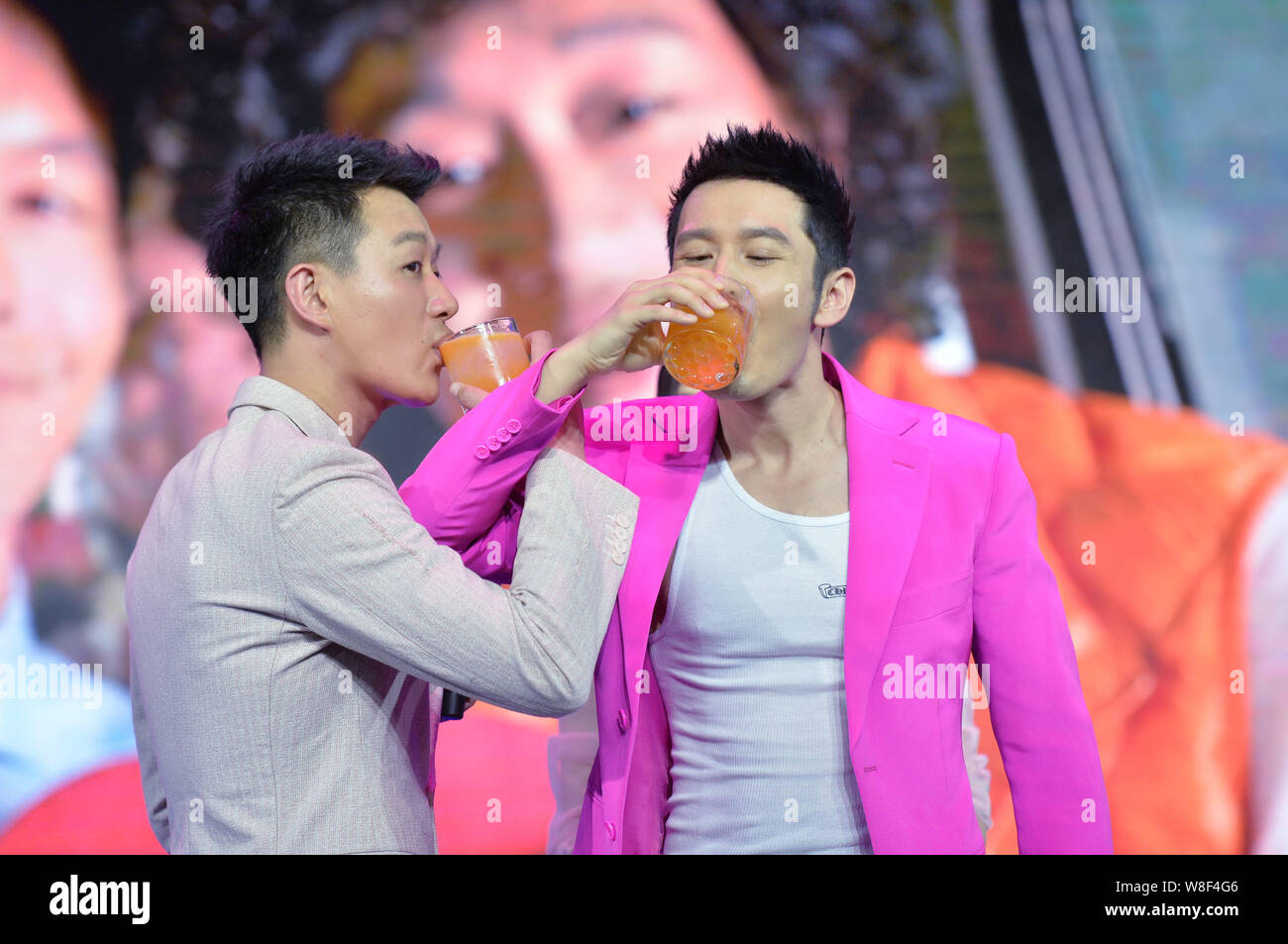 Chinese actors Tong Dawei, left, and Huang Xiaoming drink cross-cupped juice during the premiere of their new movie 'Hollywood Adventures' in Beijing, Stock Photo