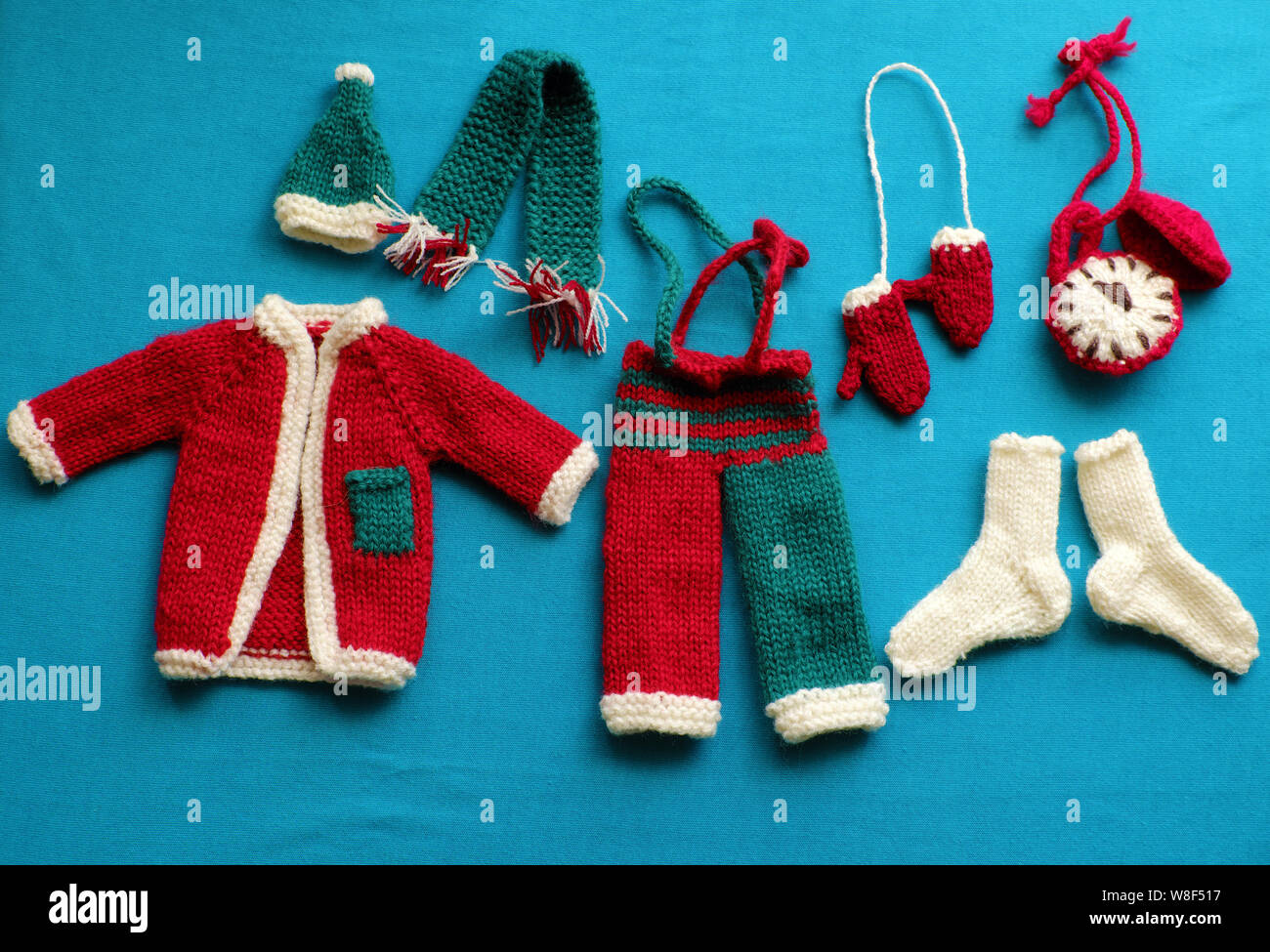 Top view of Santa clothes with accessories as gloves, hat, scarf, socks in white, red and green knit from yarn on blue background, small decorations Stock Photo