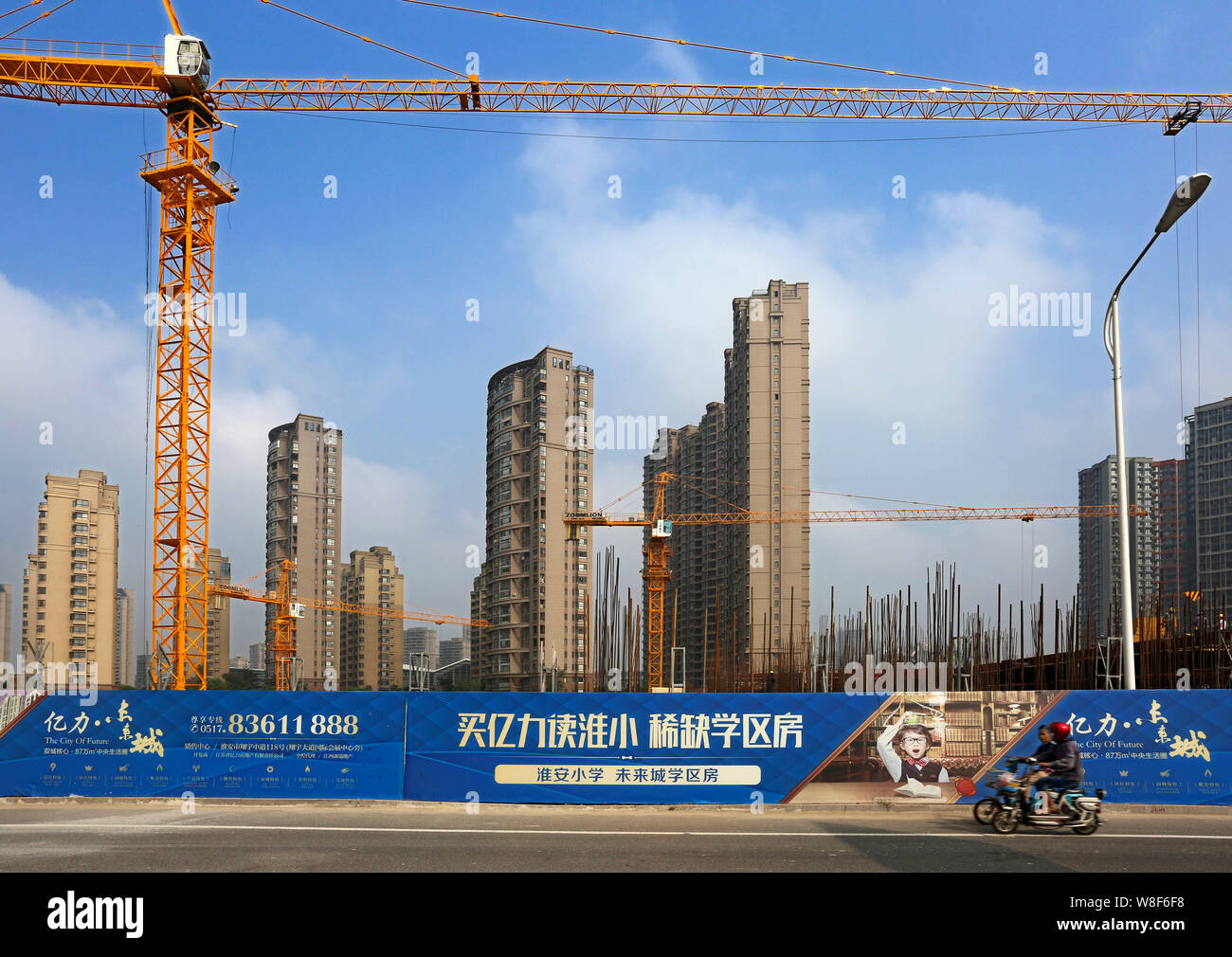 --FILE--Chinese cyclists ride their electric bike past the construction site of a residential property project in Huaian city, east China's Jiangsu pr Stock Photo