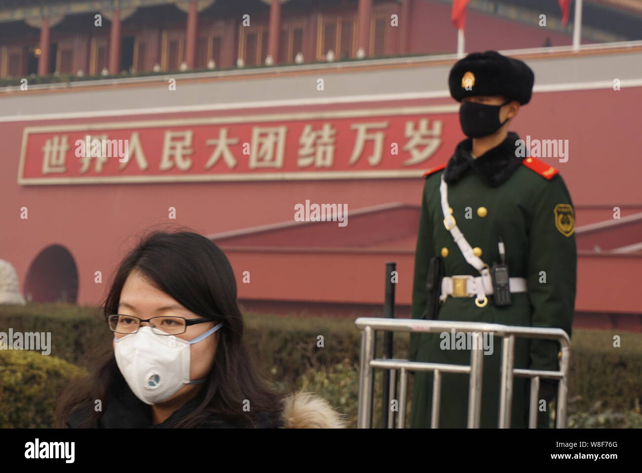 A tourist wearing a face mask walks past a masked paramilitary policeman standing guard in front of the Tiananmen Rostrum in heavy smog in Beijing, Ch Stock Photo