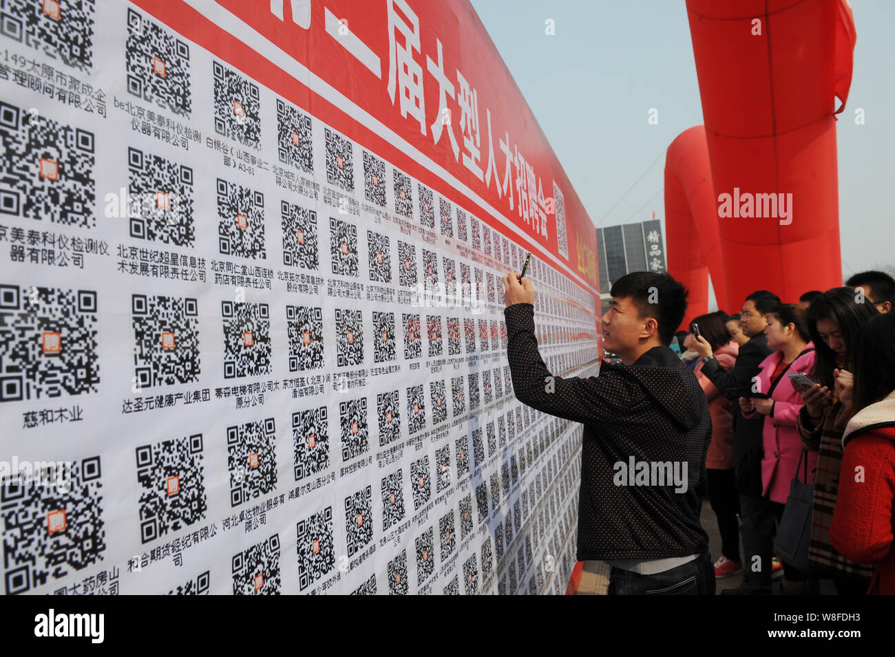 Job seekers scan QR codes on a big billboard of available jobs to