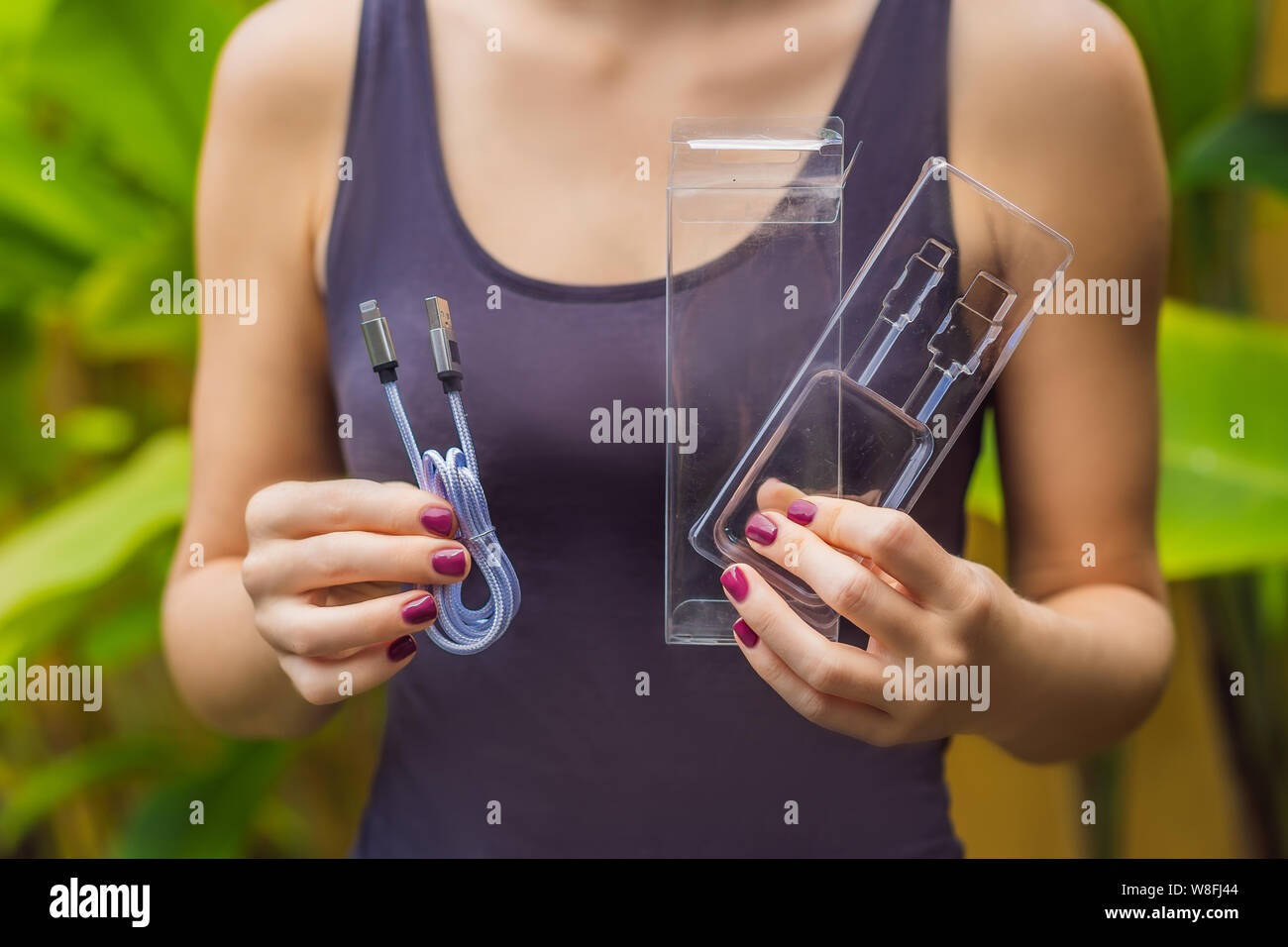 Female hands printed a new wire to charge the phone. The wire was packed in a large number of plastic packaging, which will be thrown into the trash Stock Photo