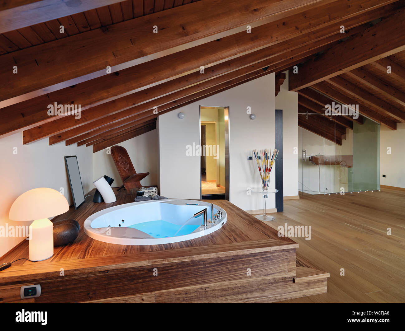 interiors shots of a modern bathroom in the attic room in the foreground the whirlpool bathtub the floor and the ceiling are made of wood Stock Photo