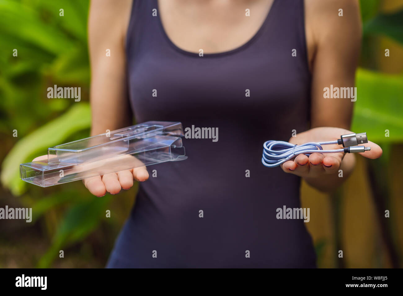 Female hands printed a new wire to charge the phone. The wire was packed in a large number of plastic packaging, which will be thrown into the trash Stock Photo