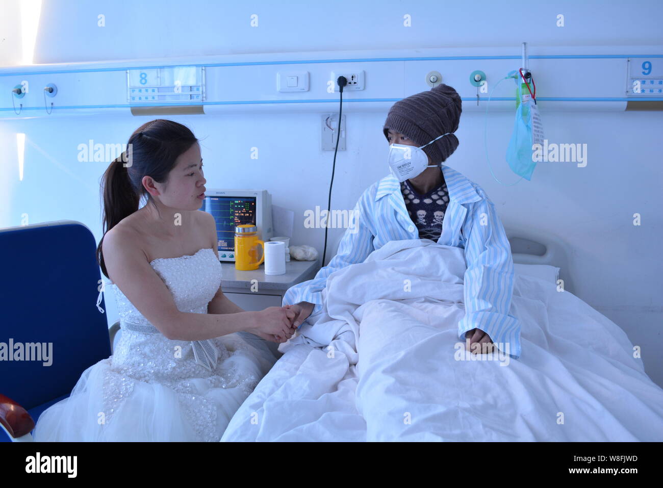 24-year-old Huang Xiju in a white wedding gown, holds the hand of her leukemia-stricken younger brother in a ward at the Kunming PLA General Hospital Stock Photo
