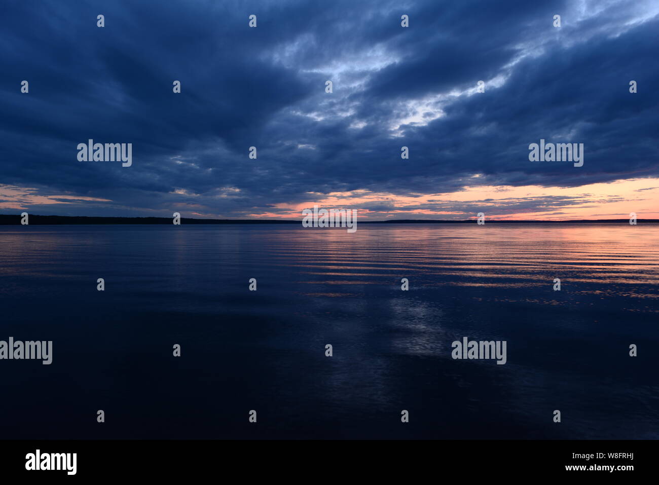 Twilight sky in bright blue clouds above a quiet surface of the water in the light of the setting sun before night Stock Photo