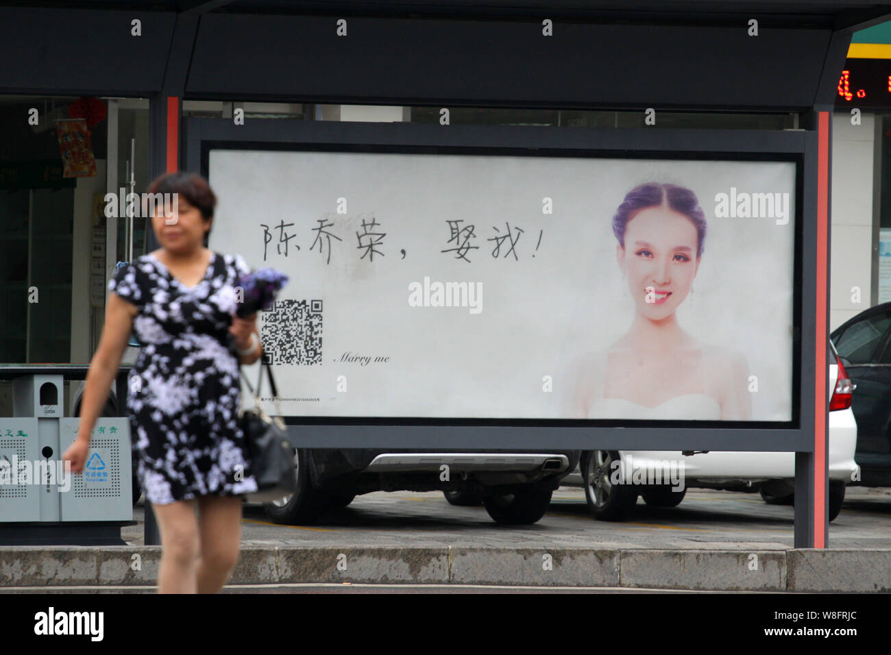 A pedestrian walks past an advertisement with a photo of a woman wearing her wedding dress and Chinese characters, which means "Chen Qiaorong, Marry m Stock Photo