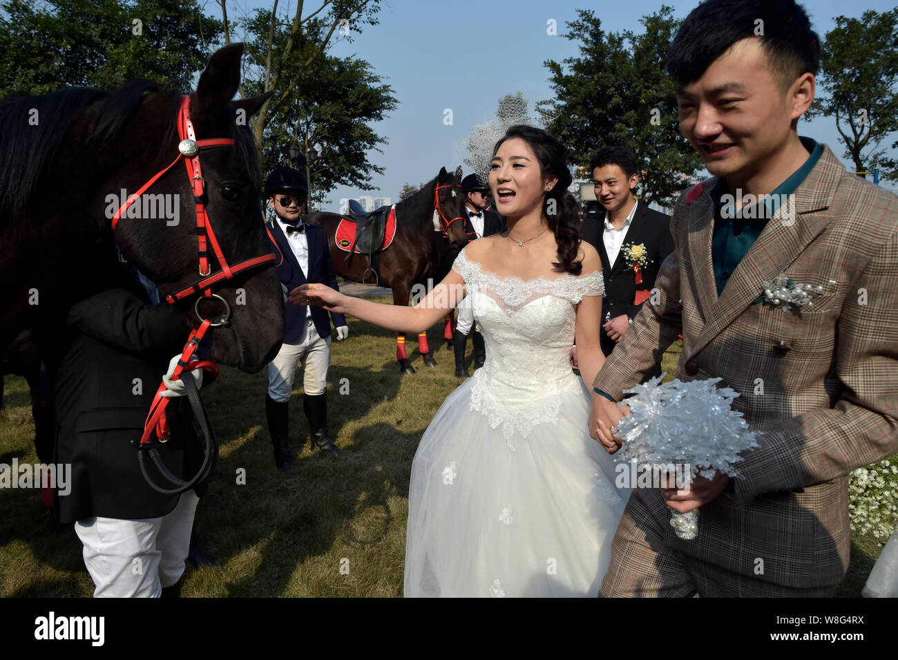 A newlywed couple who are both horse lovers walk past equestrians with horses during their wedding ceremony in Chongqing, China, 7 March 2015.   A new Stock Photo