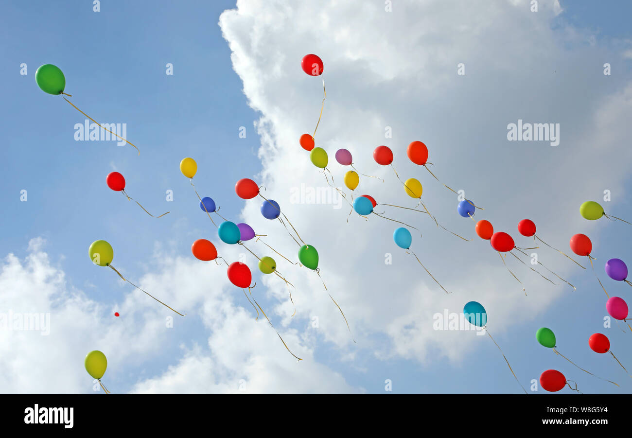 dozen of balloons in the blue sky with many clouds symbol of joy and happiness and carefreeness after the party Stock Photo
