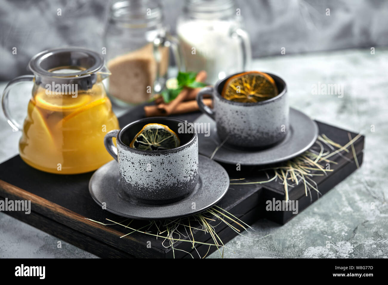 Transparent glass teapot with chitrus tea and cups, tea set on a wooden table. Close up, gray background, soft light. Stock Photo