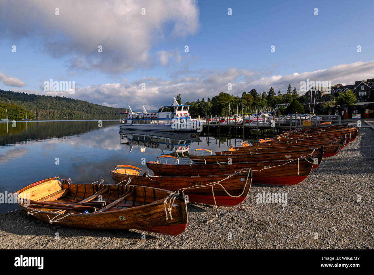 A lake cruiser and rowing boats lined up ready along the promenade at Bowness-on-Windermere Stock Photo