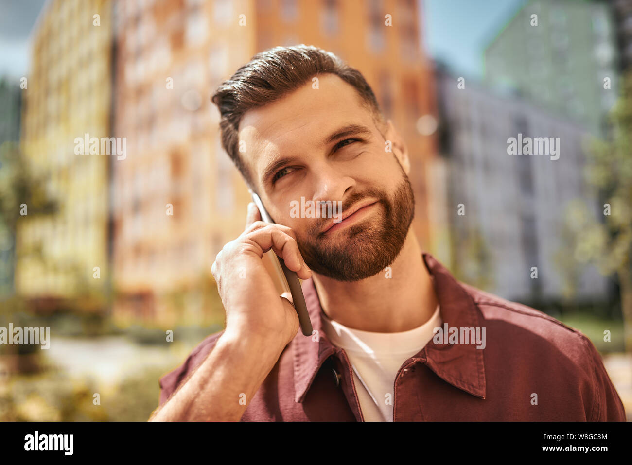 I don't know. Portrait of thoughtful bearded man talking by phone while standing on the street. Doubt concept. Digital. Communication Stock Photo