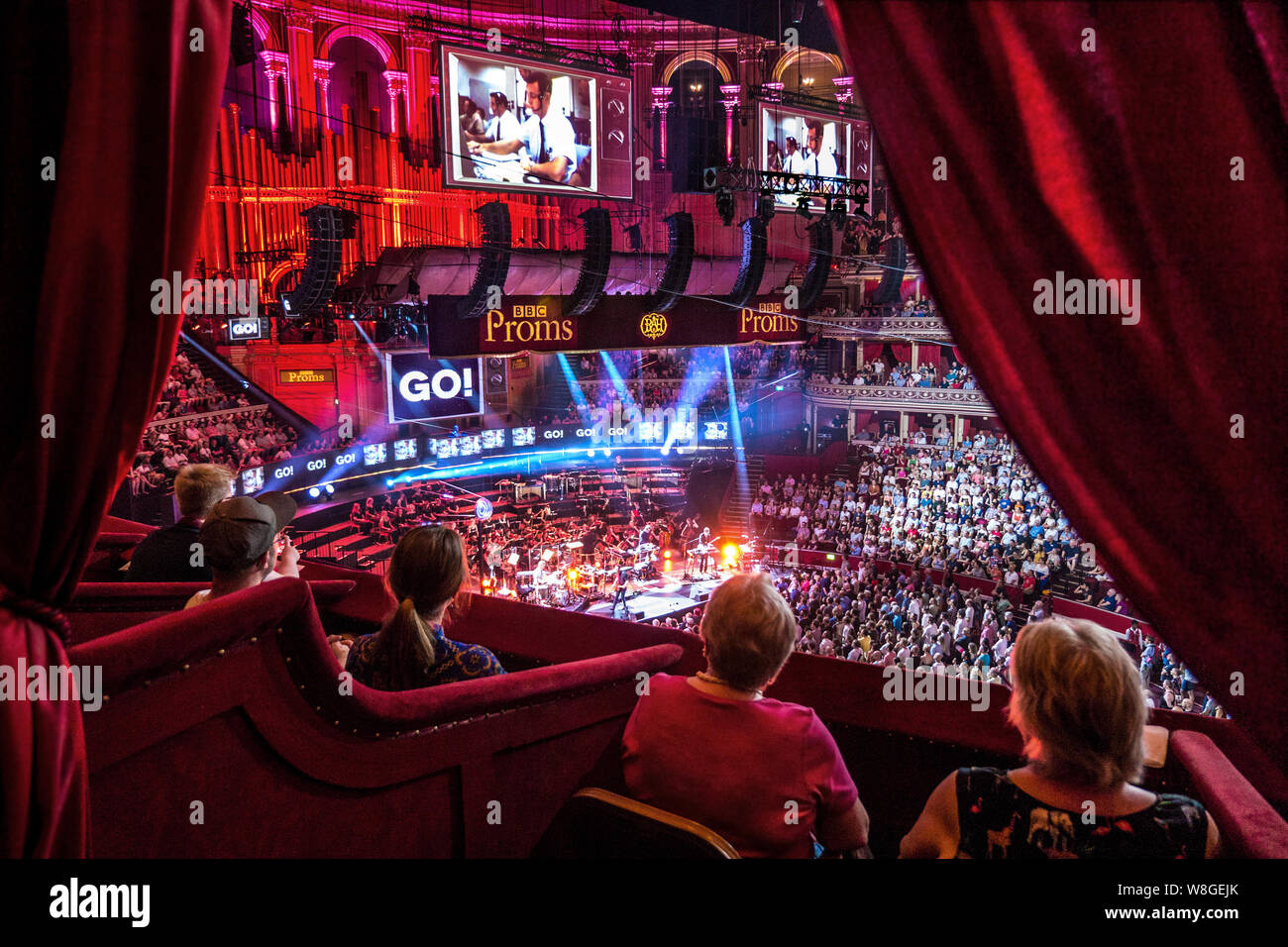 The Royal Albert Hall Audience BBC Proms performance interior viewed from luxury plush private box in auditorium with, sound & spectacular light effects with dramatic eclectic music performance by 'Public Service Broadcasting' and The Multi-Story Orchestra of a work entitled 'The Race For Space' an audio visual spectacular honouring mans achievements in space. Proms Promenade Concerts Royal Albert Hall Kensington London UK Stock Photo