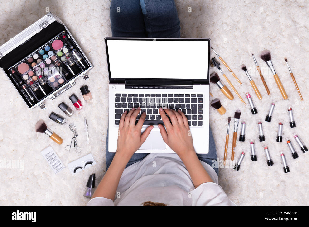 An Overhead View Of Woman Sitting On Rug While Using Laptop Near Beauty Product Stock Photo