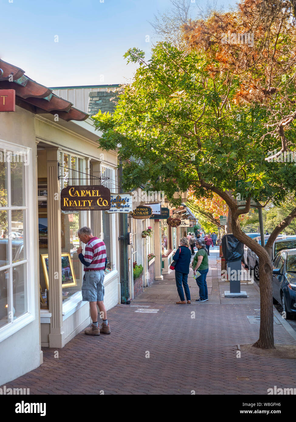 Carmel by the Sea view down Dolores Street in autumnal colour with male visitor browsing houses for sale and rent at Carmel Realty Company and shoppers behind Carmel by the Sea Monterey California USA Stock Photo
