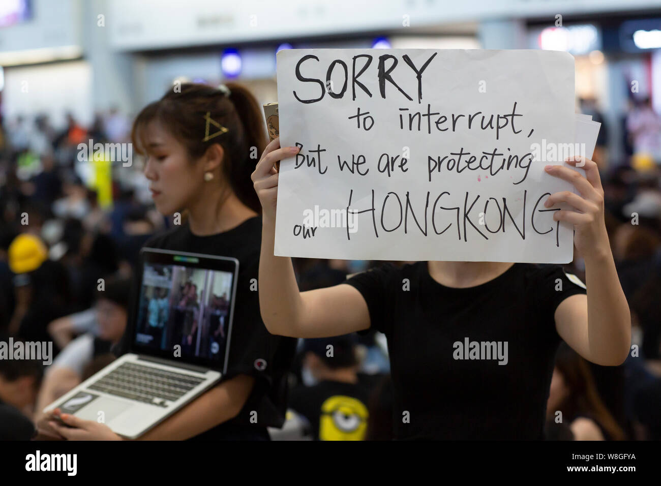 A female protester holding a message to apologise to the travellers for the inconvenience they have causes due to the protest.Thousands of protesters took to the arrival hall of the Hong Kong international airport under the name 'Greetings from HKers Assembly' to catch the attention by the international travelers who just landed in Hong Kong about the current unrest situation in the city. Stock Photo