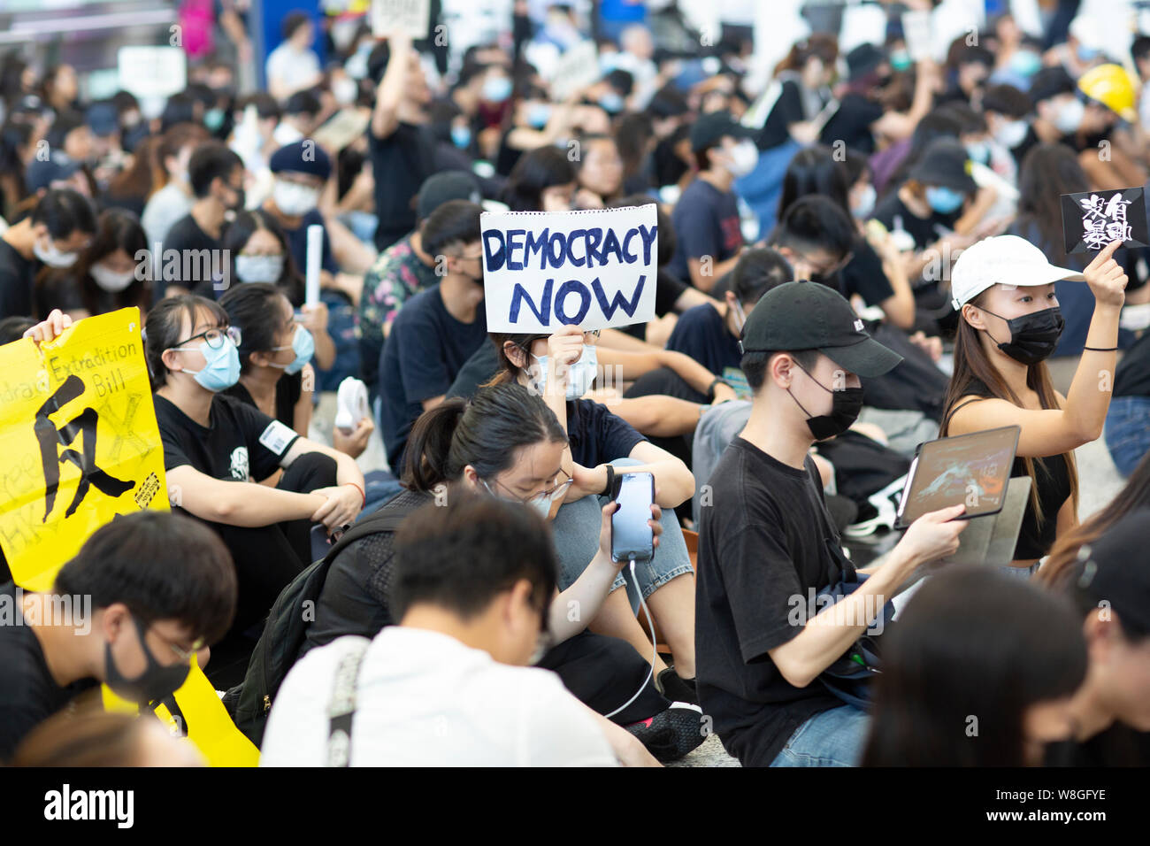 A protester holds a placard reads 'Democracy now' during the demonstration in the airport.Thousands of protesters took to the arrival hall of the Hong Kong international airport under the name 'Greetings from HKers Assembly' to catch the attention by the international travelers who just landed in Hong Kong about the current unrest situation in the city. Stock Photo