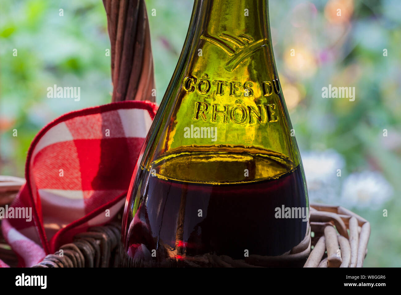 Cotes du Rhone red wine bottle in rustic wicker picnic basket, alfresco  drinks drinking with typical French chequered napkin, in late afternoon sun  sunset summer shade garden behind, holiday vacation wine tasting