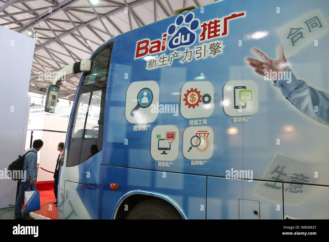 --FILE--A visitor stands next to a passenger bus with an advertisement for Baidu during the 16th China International Industry Fair (CIIF) in Shanghai, Stock Photo