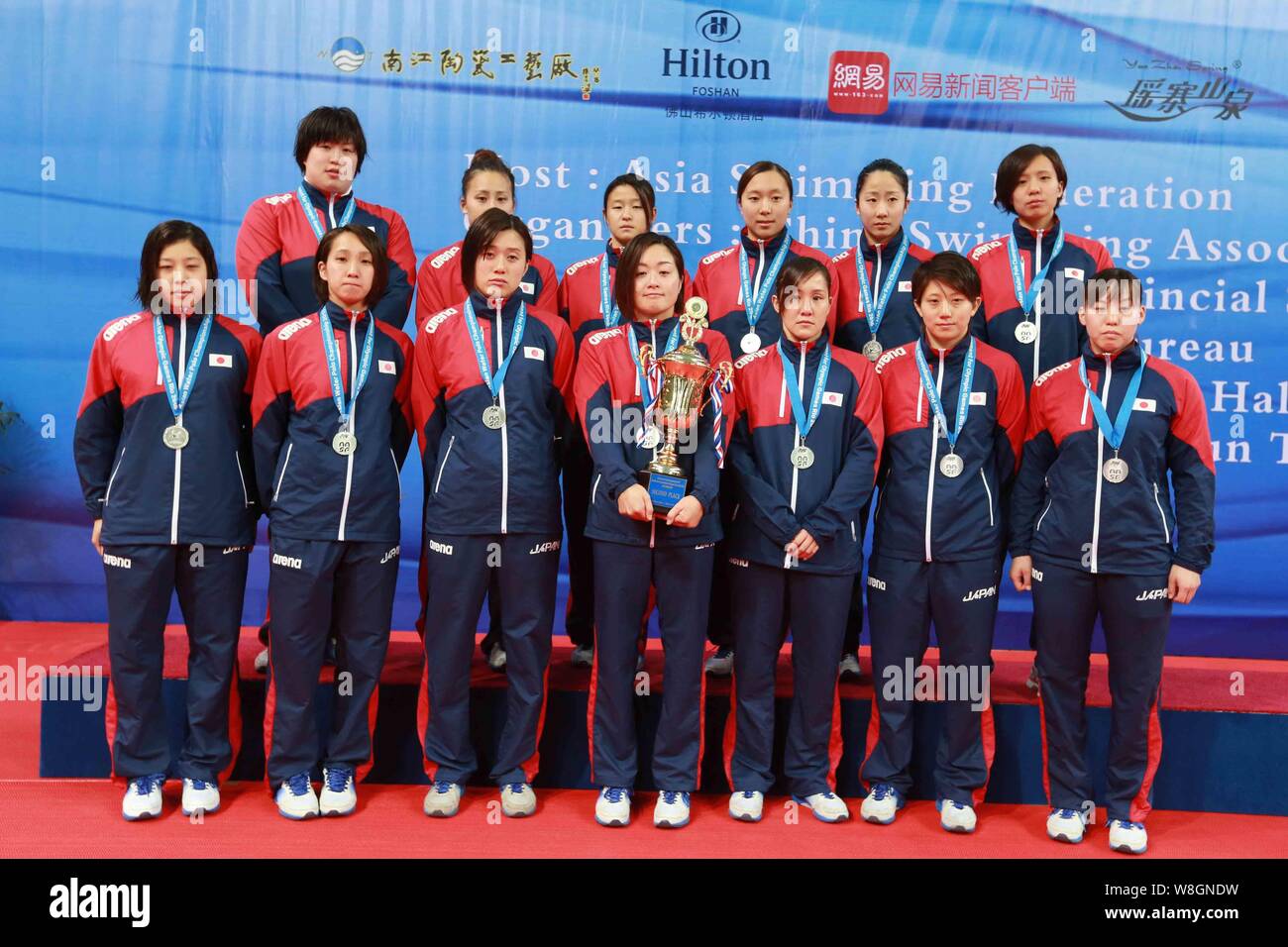 Players of Japan women's national water polo team pose with the trophy on the podium after being