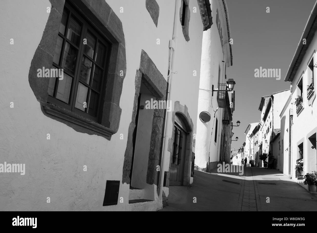 Low angle view of white houses along a narrow street in Begur. Two children walk away in the distance. Black and white wide-angle photo. Stock Photo