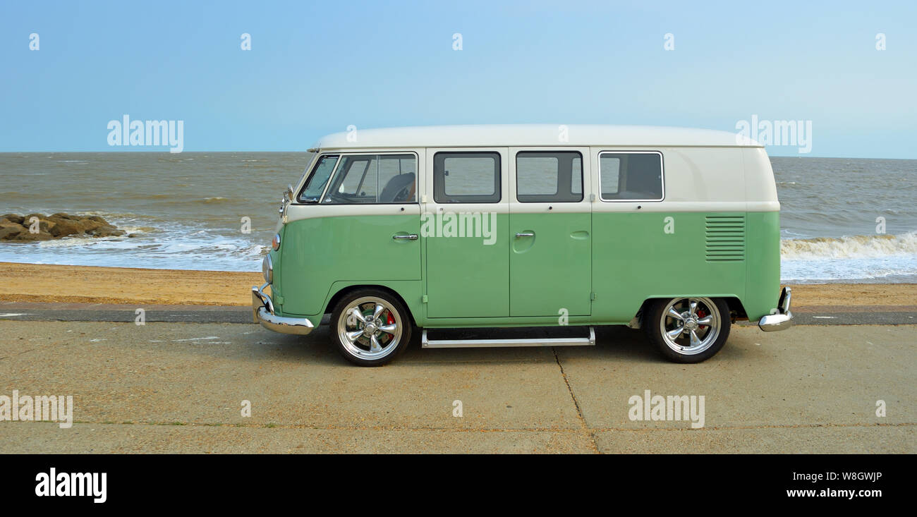 Classic Green and white  VW Camper Van parked on Seafront Promenade. beach and sea in the background Stock Photo