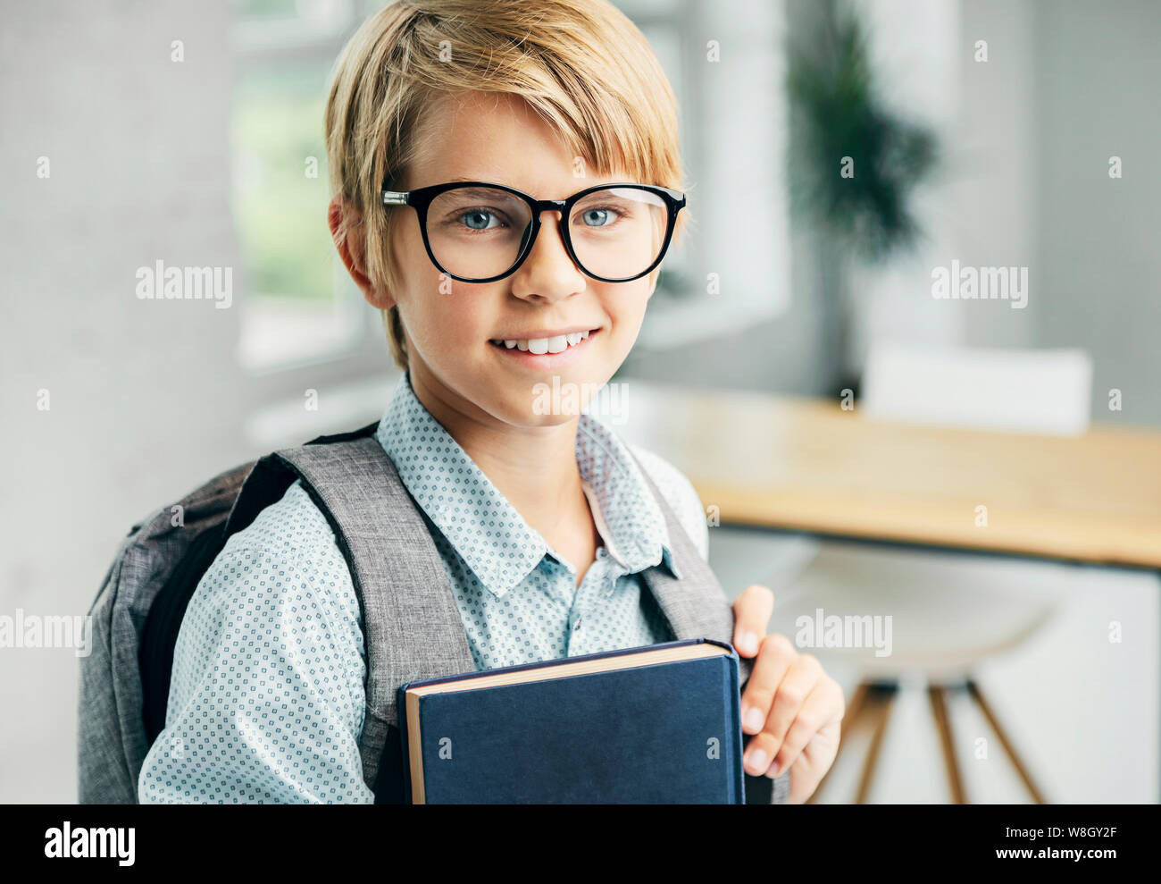 Smiling blond boy holding books in a classroom Stock Photo