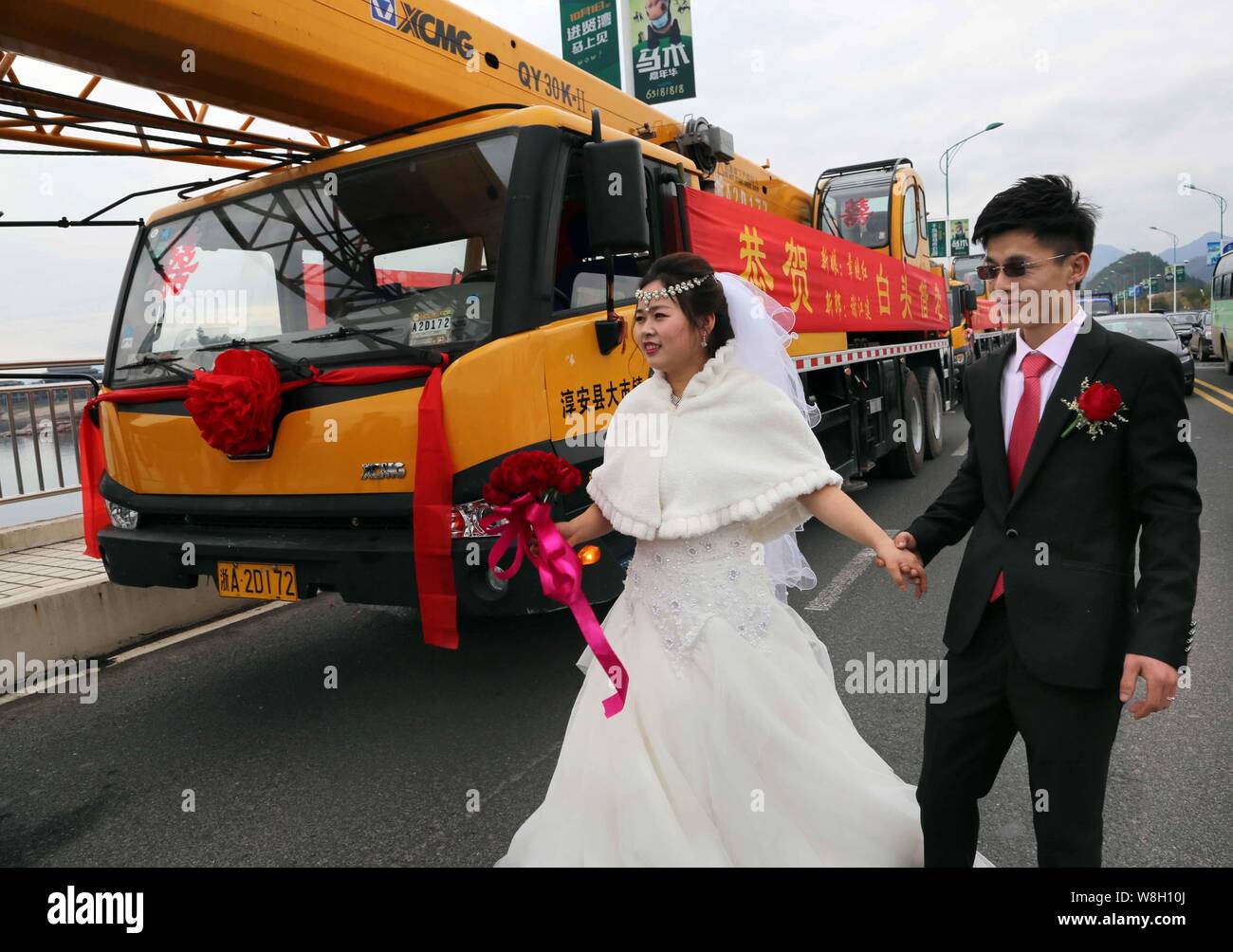 Chinese groom Xie Jiangjian, right, and his bride walk hand in hand past a motorcade of crane trucks on a bridge on the way to their wedding in Chun'a Stock Photo