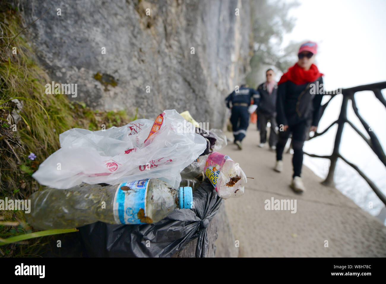 Chinese tourists walk past a garbage bin full of the litter collected by cleaning workers on the cliff of Tianmen Mountain or Mount Tianmenshan in Zha Stock Photo
