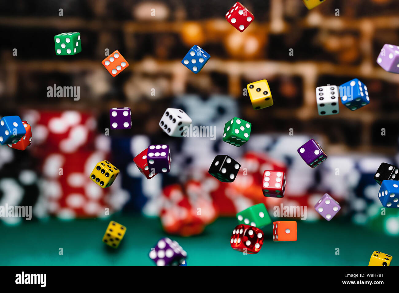 Multicolored dice Chips cascading in front of a background of stacked poker chips.  Depth of field is medium, so many dice are in focus and many other Stock Photo