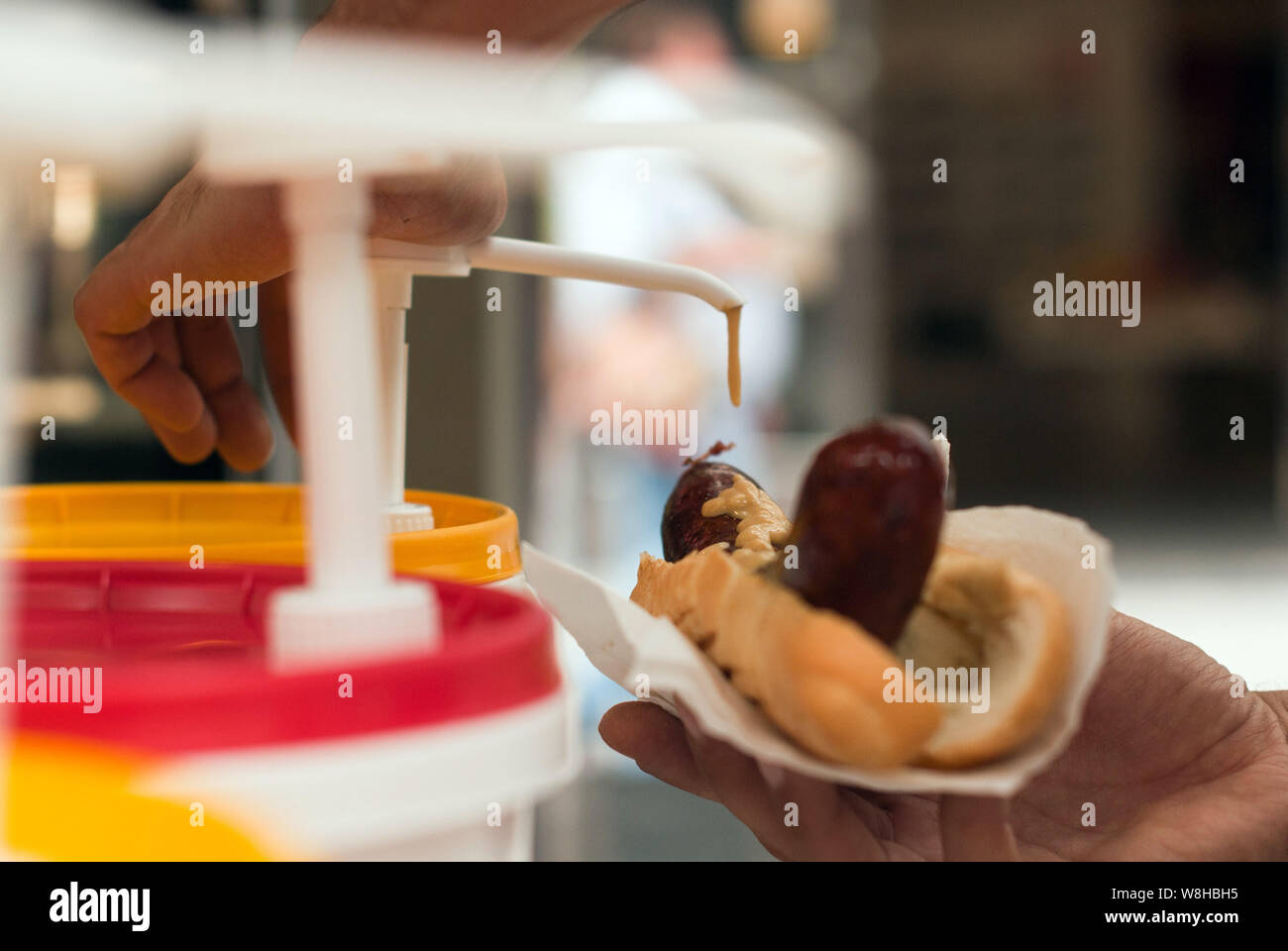Pouring mayonnaise on the hot-dog, tasteful snack while traveling. Stock Photo