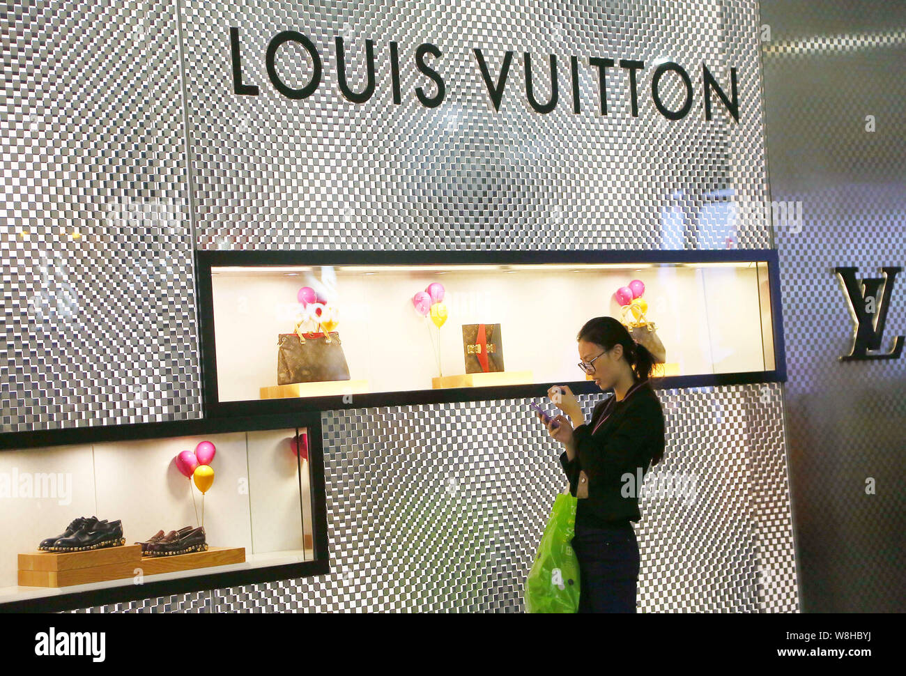 FILE--A pedestrian using her smartphone walks past a Louis Vuitton boutique of LVMH Moet Louis Vuitton SA in Hong Kong, China, 28 November Photo - Alamy