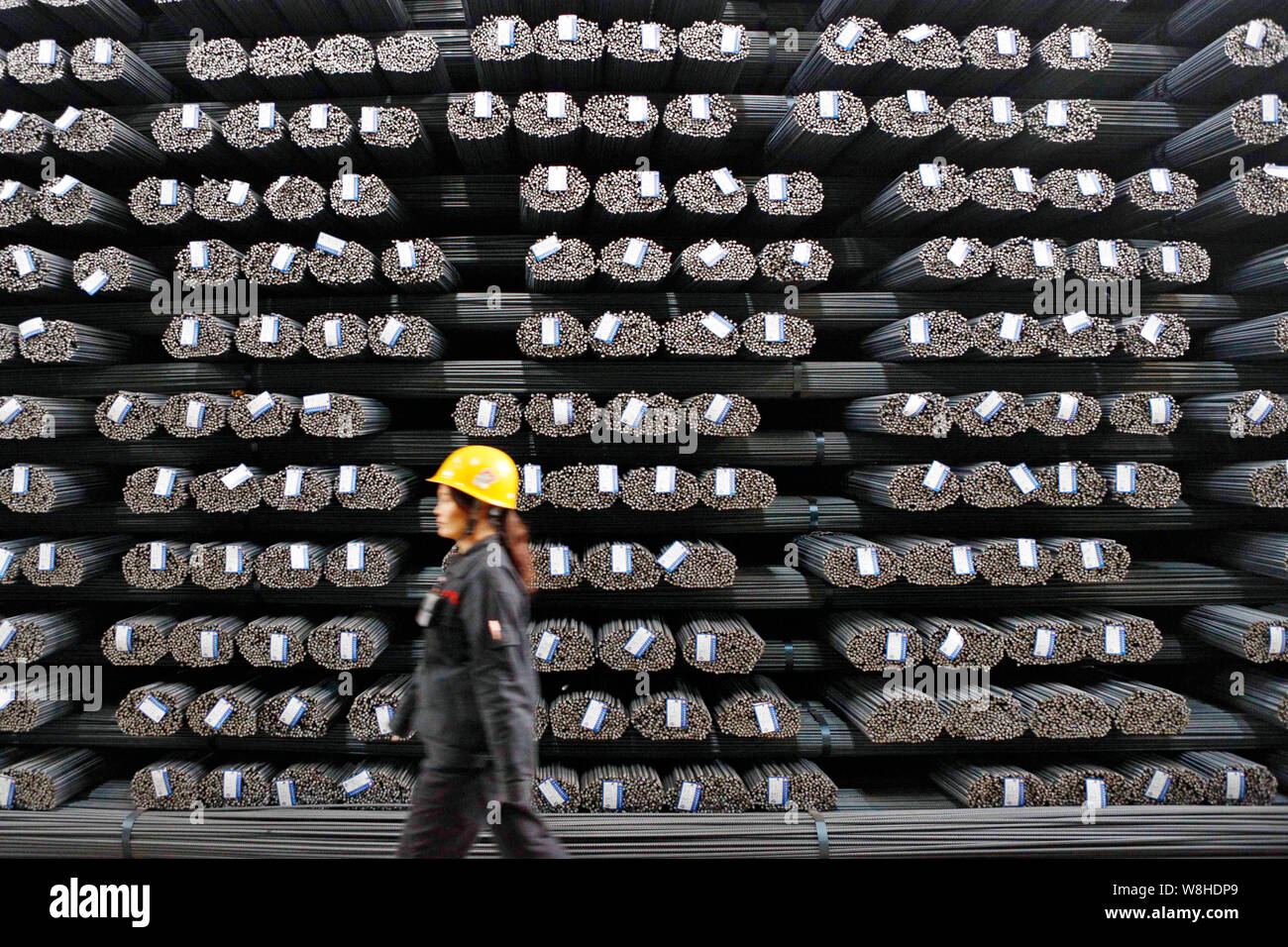 Chinese Rods System A female Chinese worker walks past stacks of reinforcing steel rods at ...