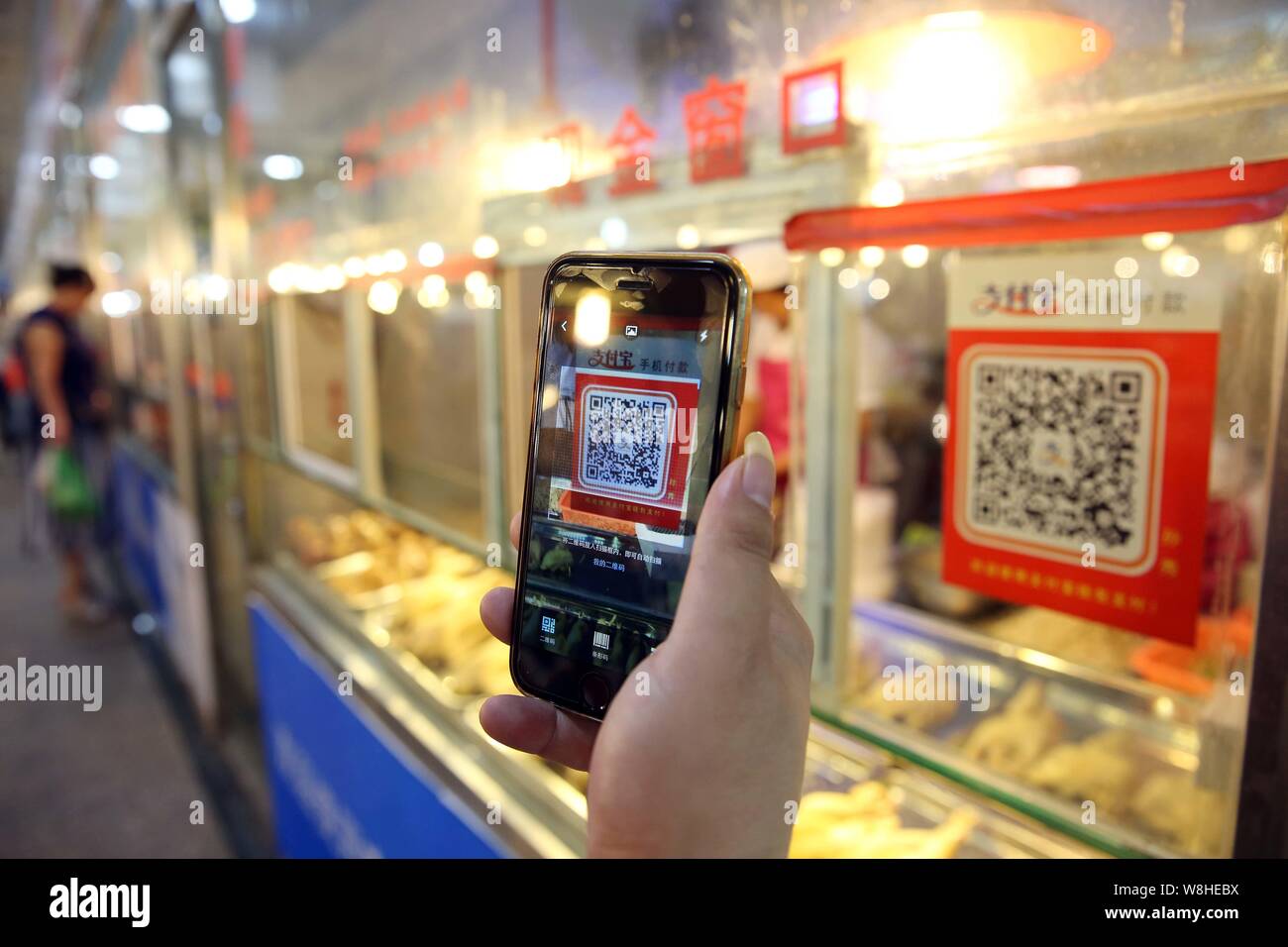 A Chinese customer scans a QR code via mobile payment service Alipay of Alibaba Group on her smartphone to pay for her purchase at a free market in We Stock Photo