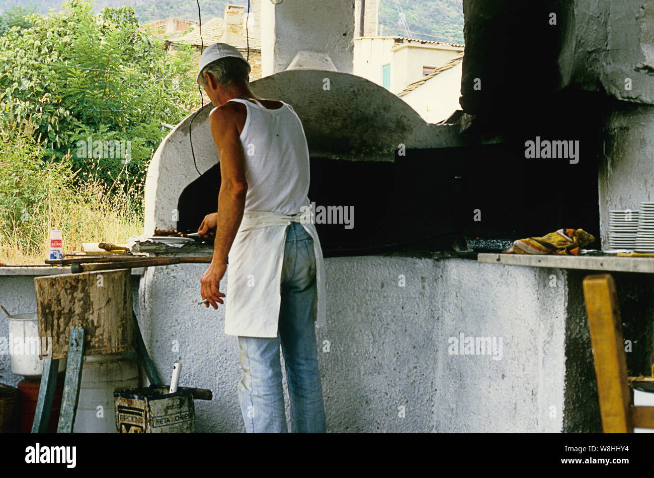 Taverna chef ignores basic health and safety procedures by smoking whilst preparing food in an outdoor kitchen in Skala Potamias, Thassos, Greece. Stock Photo
