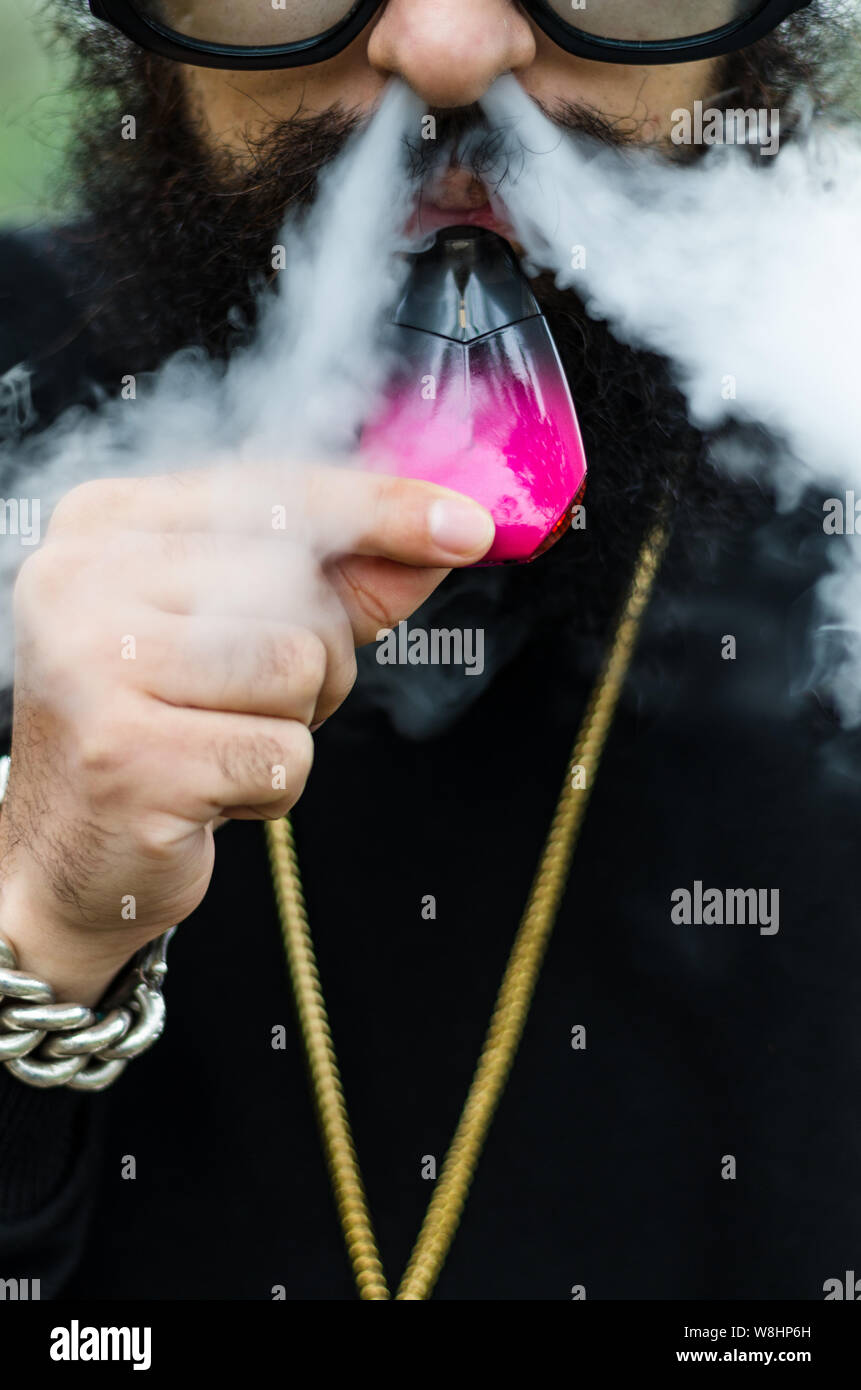 Close-up of a man with an electronic cigarette, man with leafy beard, gold chain and sunglasses Stock Photo