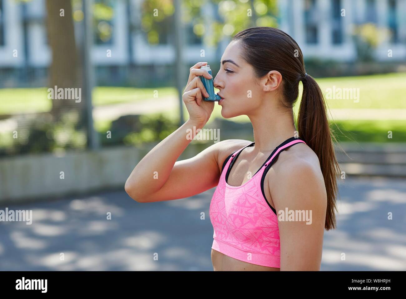 Young woman in sports crop top using an inhaler. Stock Photo