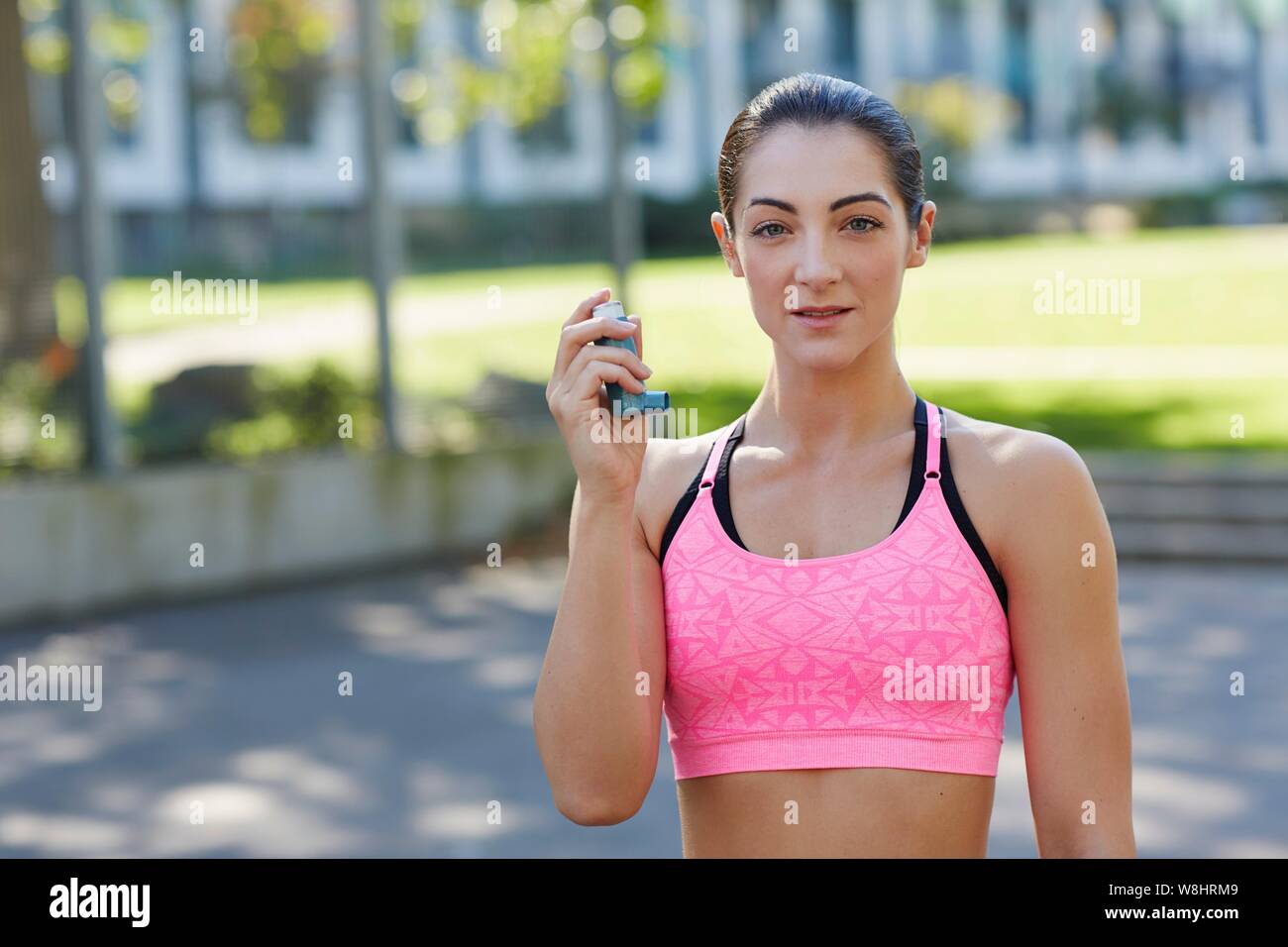Young woman in sports crop top holding an inhaler. Stock Photo