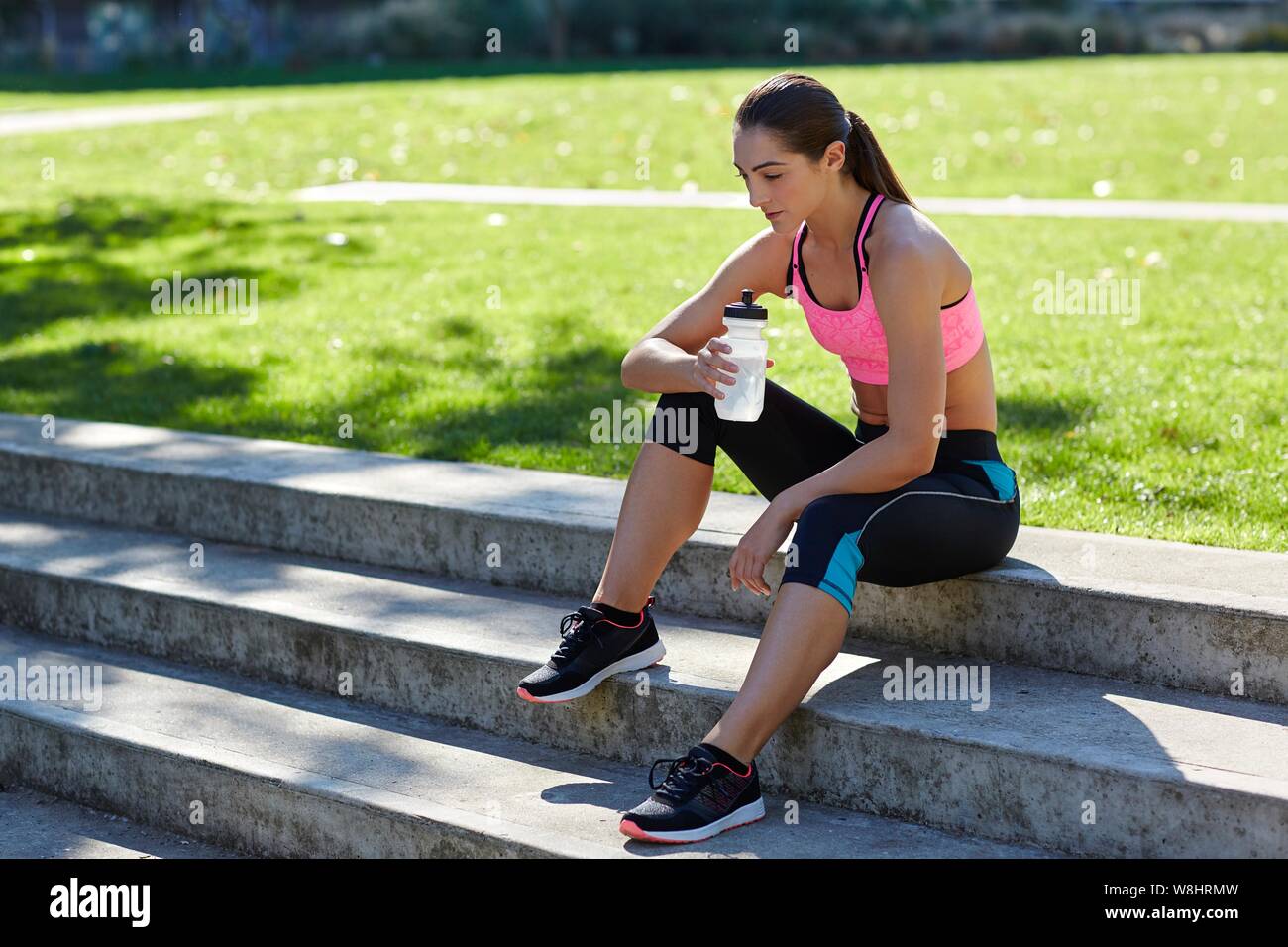 Young woman in sports clothing resting on steps with water bottle. Stock Photo