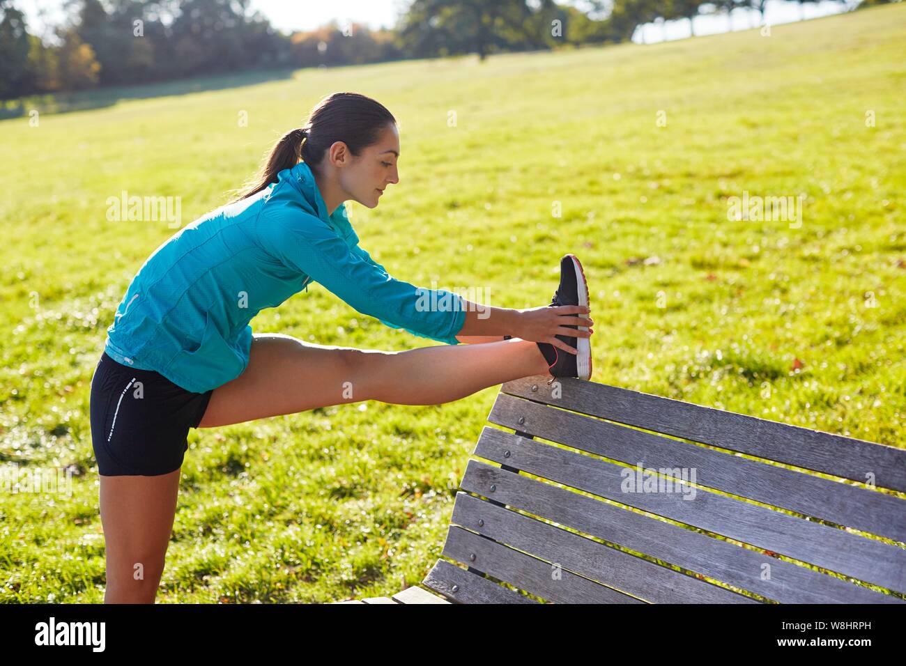 Young woman stretching leg on park bench. Stock Photo