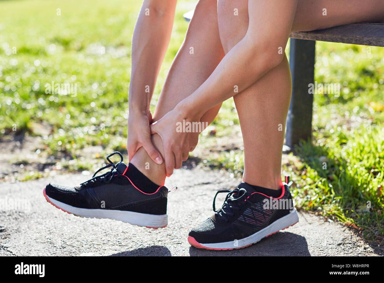 Woman wearing trainers holding her ankle. Stock Photo
