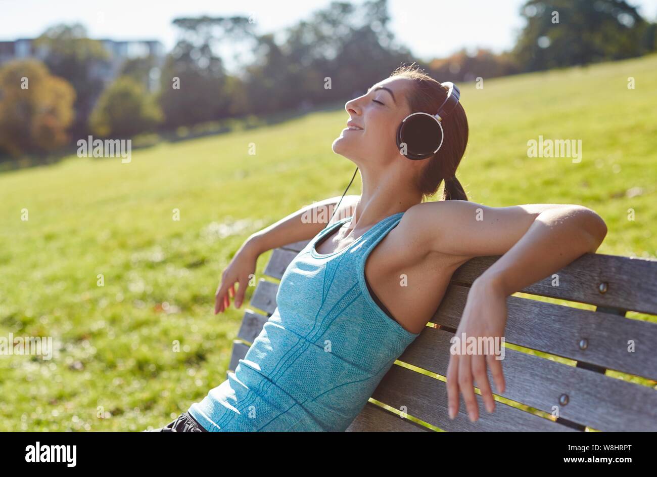 Young woman listening to music from smart phone, sitting on a bench. Stock Photo