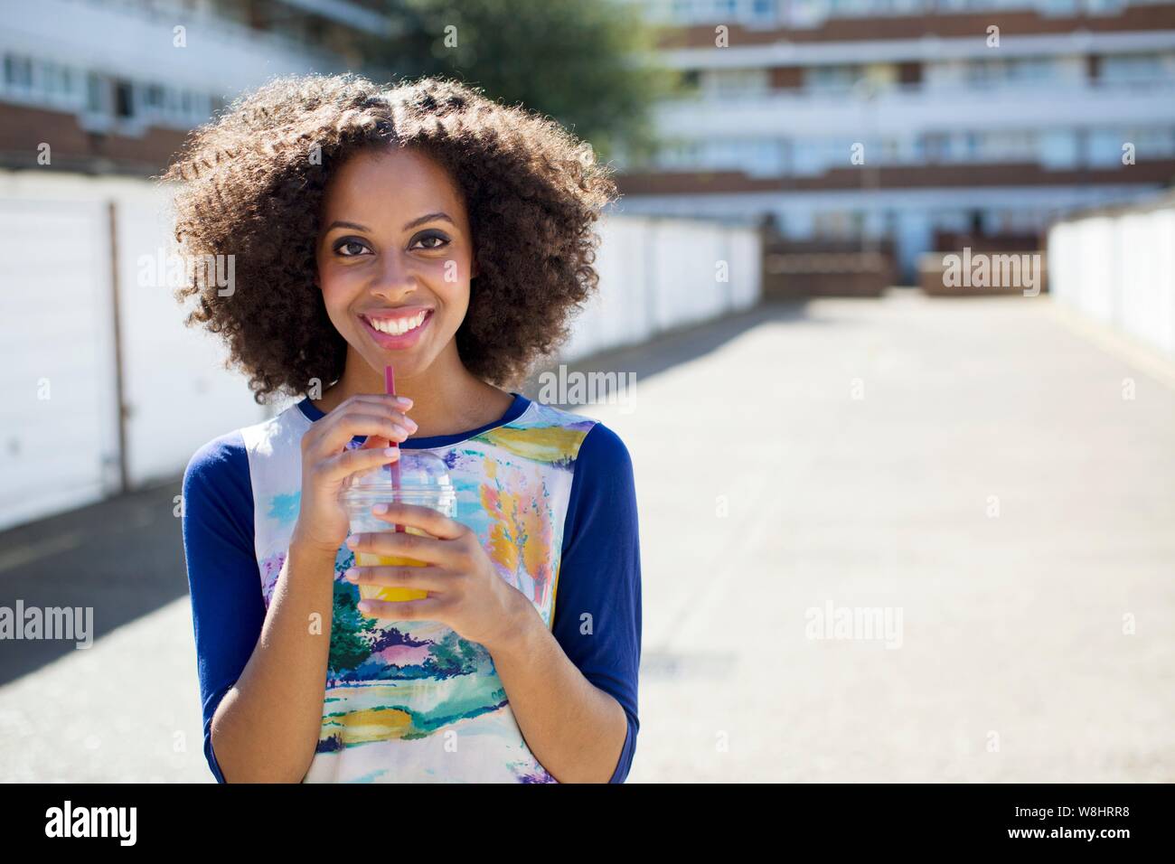 Young woman with drink outdoors, smiling. Stock Photo