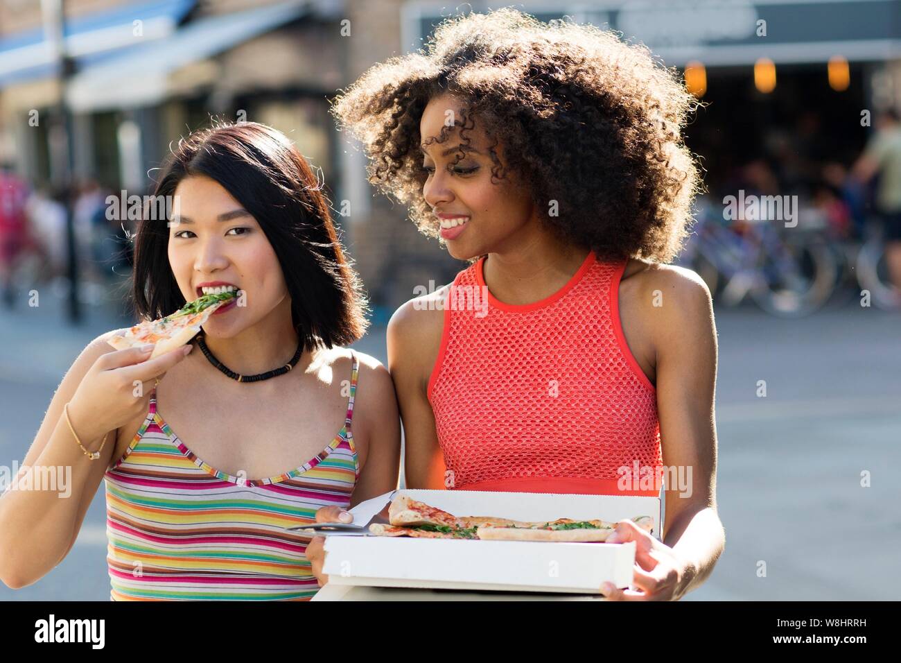 Two young women eating pizza from box outdoors. Stock Photo
