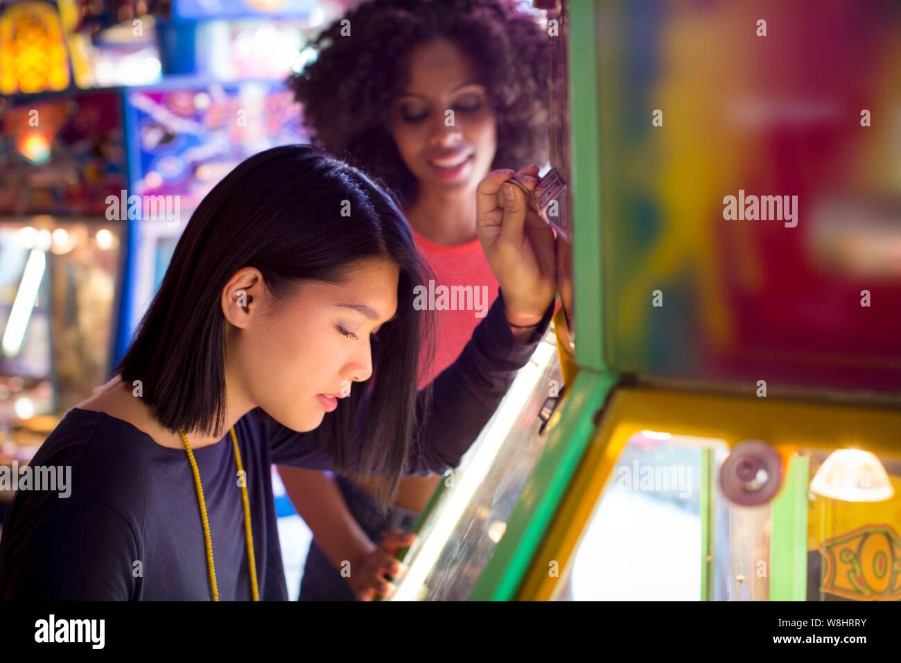 Two young women playing arcade game at fun fair. Stock Photo