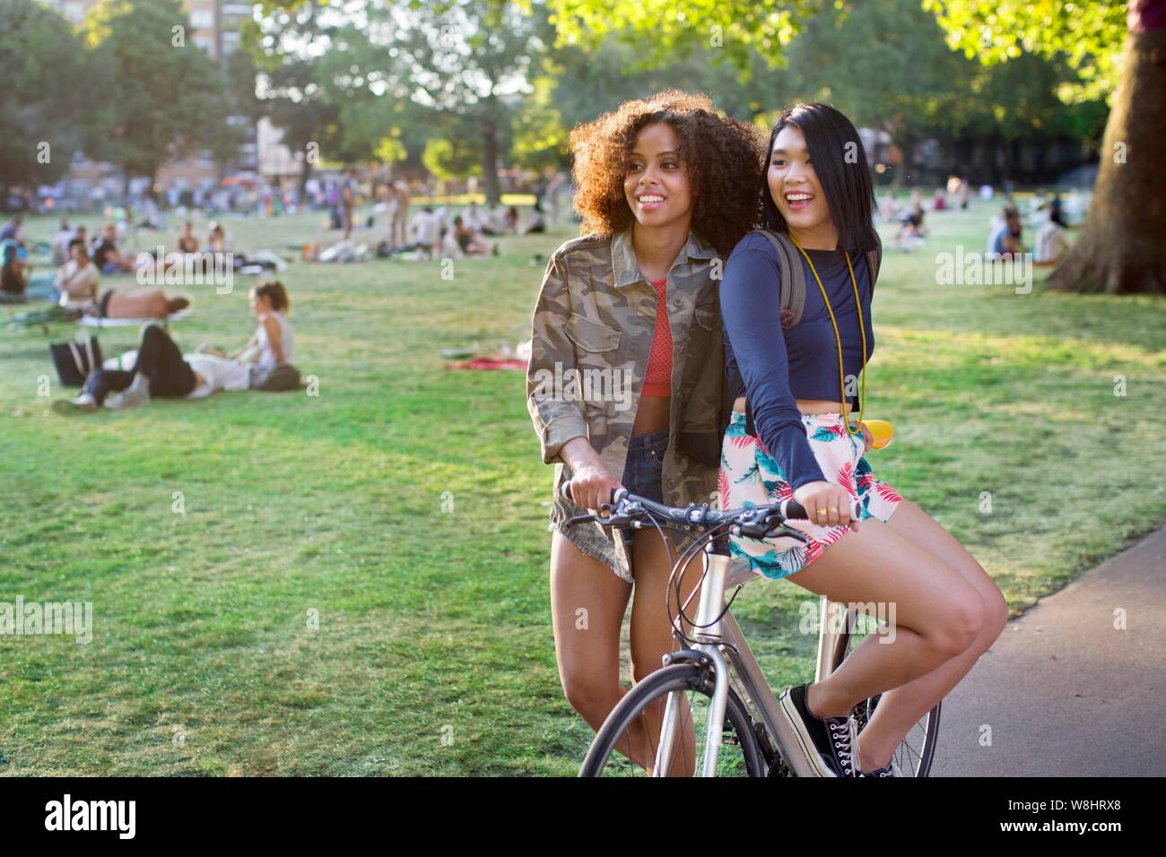 Two young women in park, one sitting on bicycle. Stock Photo