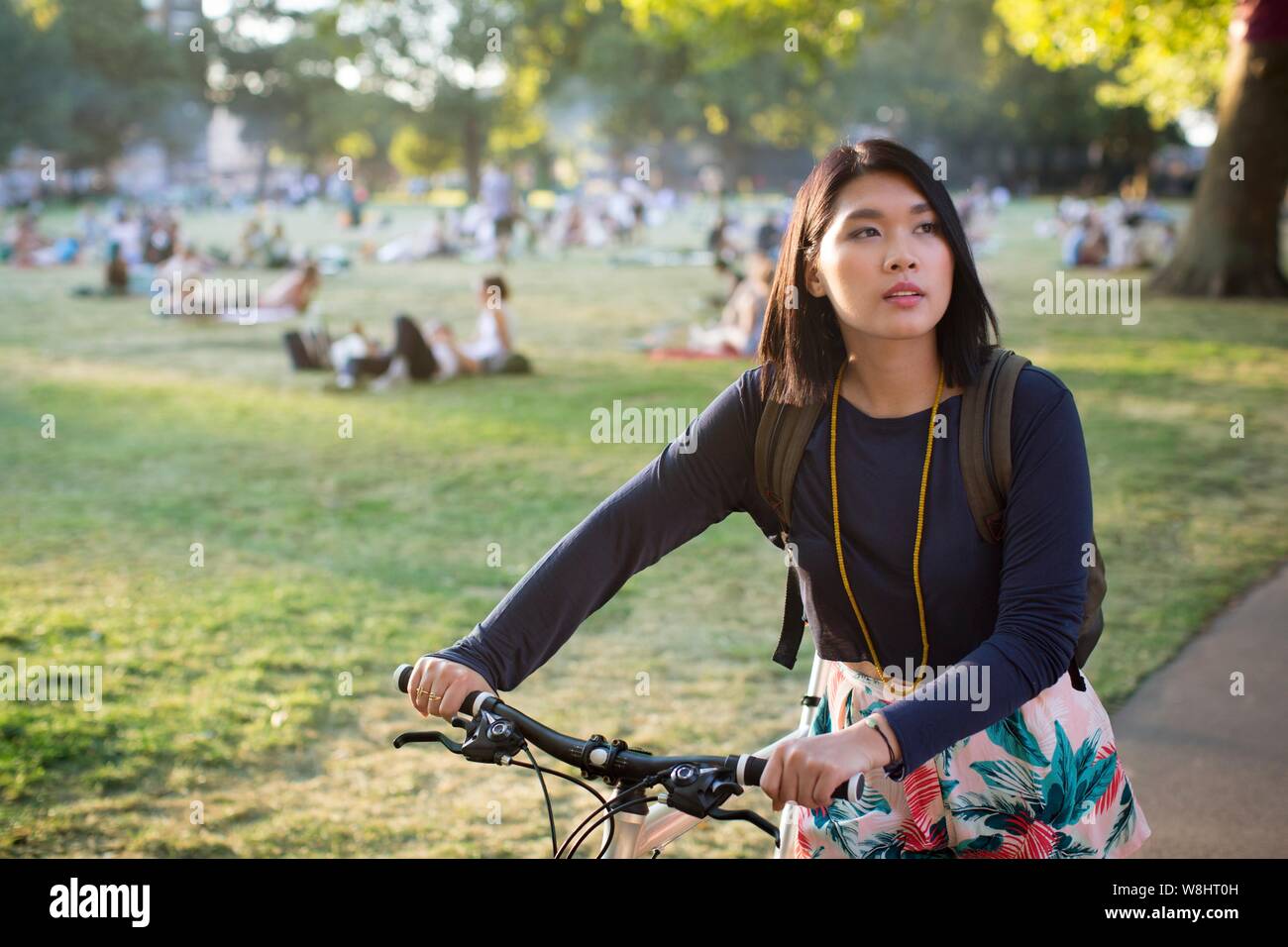 Young woman pushing bicycle in park. Stock Photo