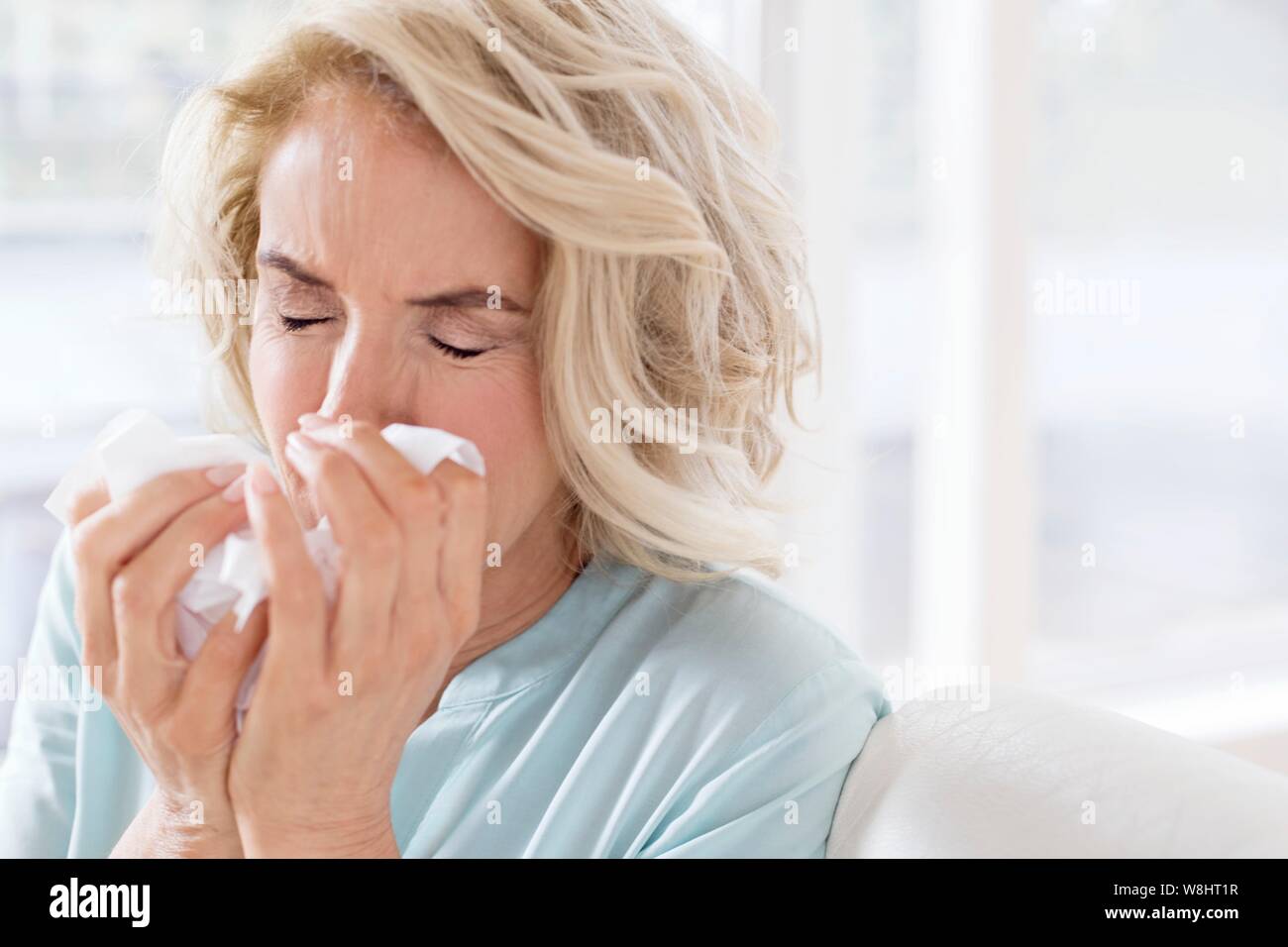 Mature woman blowing nose on tissue. Stock Photo